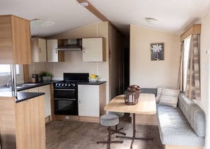 A compact kitchen with a stove, oven, and sink, a small dining table with a chair, and a sofa in a living area.