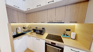 A modern kitchen with white cabinets, a black induction cooktop, a built-in oven, and a microwave. - Apartment TOP center Sofia, 5 Corners (Sofia)