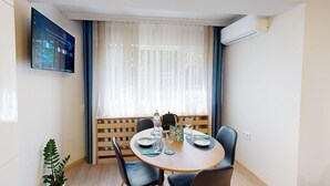 A dining area with a round table, four chairs, a potted plant, and a mounted TV displaying a YouTube interface. - Apartment TOP center Sofia, 5 Corners (Sofia)