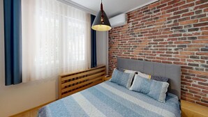 A bedroom with a brick wall, a bed with a grey headboard, and a hanging light fixture. - Apartment TOP center Sofia, 5 Corners (Sofia)
