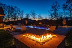 Una fogata, mobiliario exterior y una piscina iluminada.