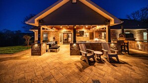 A house with a covered outdoor kitchen, stone fireplace, and outdoor seating area.