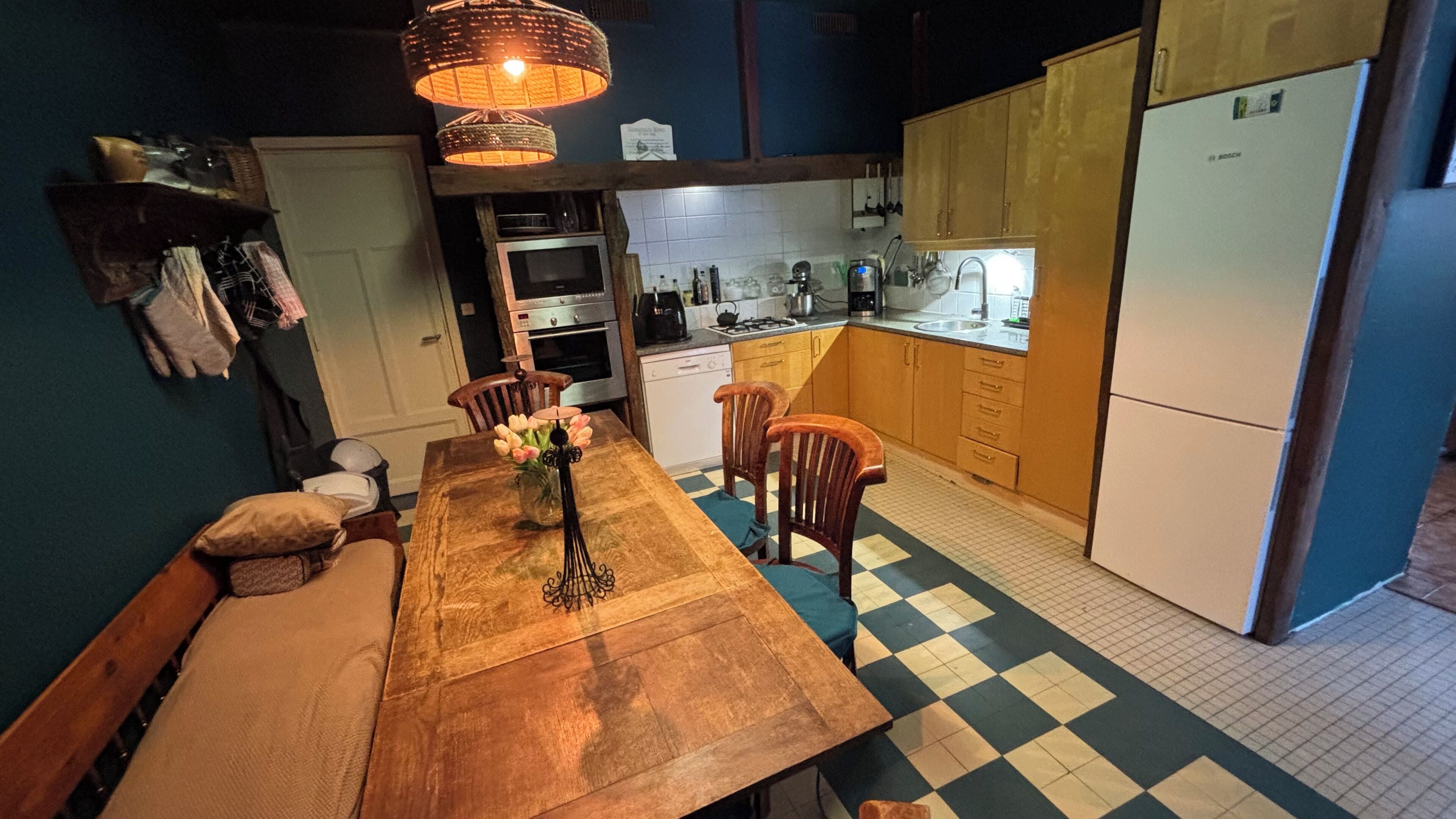 Une cuisine avec une table en bois, des chaises, un vase de fleurs et un réfrigérateur de la marque Bosch.