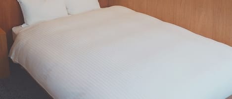 A neatly made bed with a wooden headboard, a bedside table, and a wall-mounted lamp.