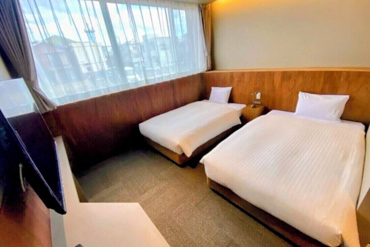 A hotel room with two beds, a desk, and a window with curtains.