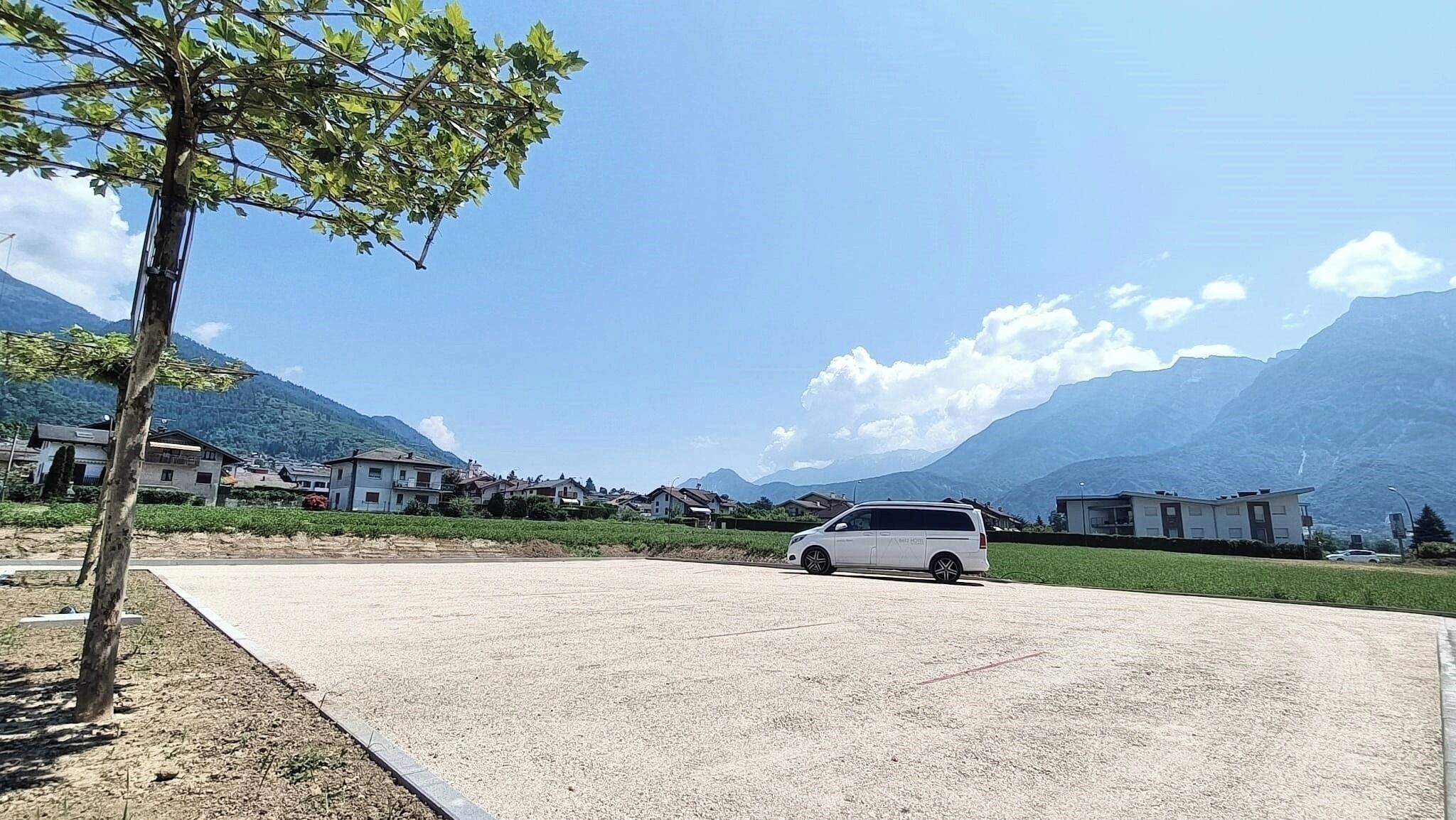 Ein Parkplatz mit einem weißen Transporter, umgeben von Gebäuden und Bergen.