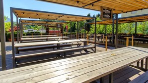 Een terras met houten tafels en banken, overdekt door een houten pergola, met borden die een restaurant aangeven.
