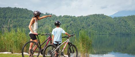 Two people with bicycles by a lake with a forested hill in the background.