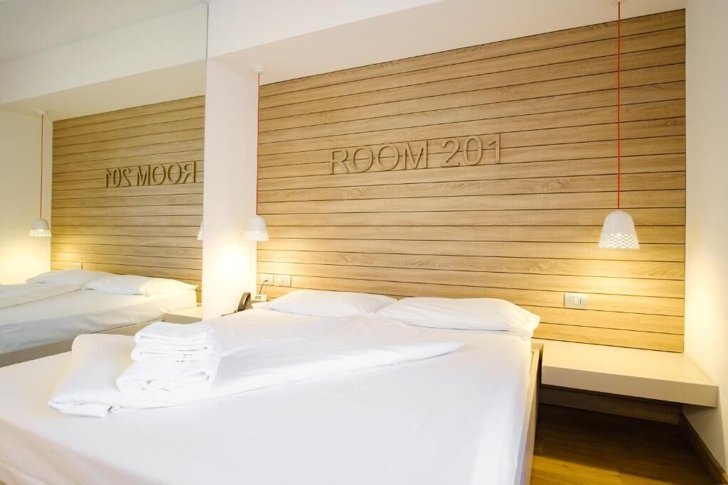 Ein Hotelzimmer mit zwei Betten, Holz-Kopfteilen und einem an der Wand befestigten Schild mit der Aufschrift 'ROOM 201'.