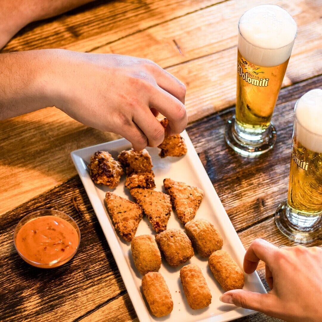 Une table en bois sur laquelle se trouvent une assiette de nourriture frite, un verre de bière et un petit bol de sauce.