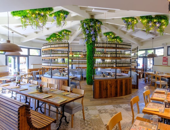 A restaurant with wooden tables, chairs, and a central bar area with shelves of bottles.