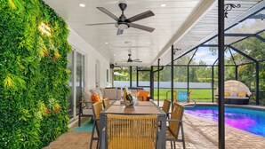A covered outdoor area with a pool, a dining table with chairs, and a ceiling fan. -  The Mimosa House • Heated Salt Water Pool + Spa • Minutes to Siesta Key (Sarasota)