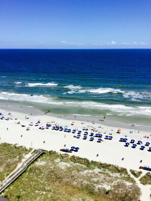 Ein Strand mit einer langen Mole, die sich ins Meer erstreckt, bewölkter Sandstrand und klarer, blauer Himmel.