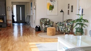 A spacious living room with a fireplace, two patterned armchairs, a round ottoman, and a glass coffee table. - 4 Star Holiday Home in Skaret (Nyhamnslage)