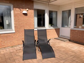 A patio with two black lounge chairs, a brick wall, and white-framed windows. - 4 Star Holiday Home in Skaret (Nyhamnslage)