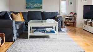 A living room with a dark grey sofa, a white coffee table with books, a grey rug, and a painting of waves on the wall. - 4 Star Holiday Home in Skaret (Nyhamnslage)