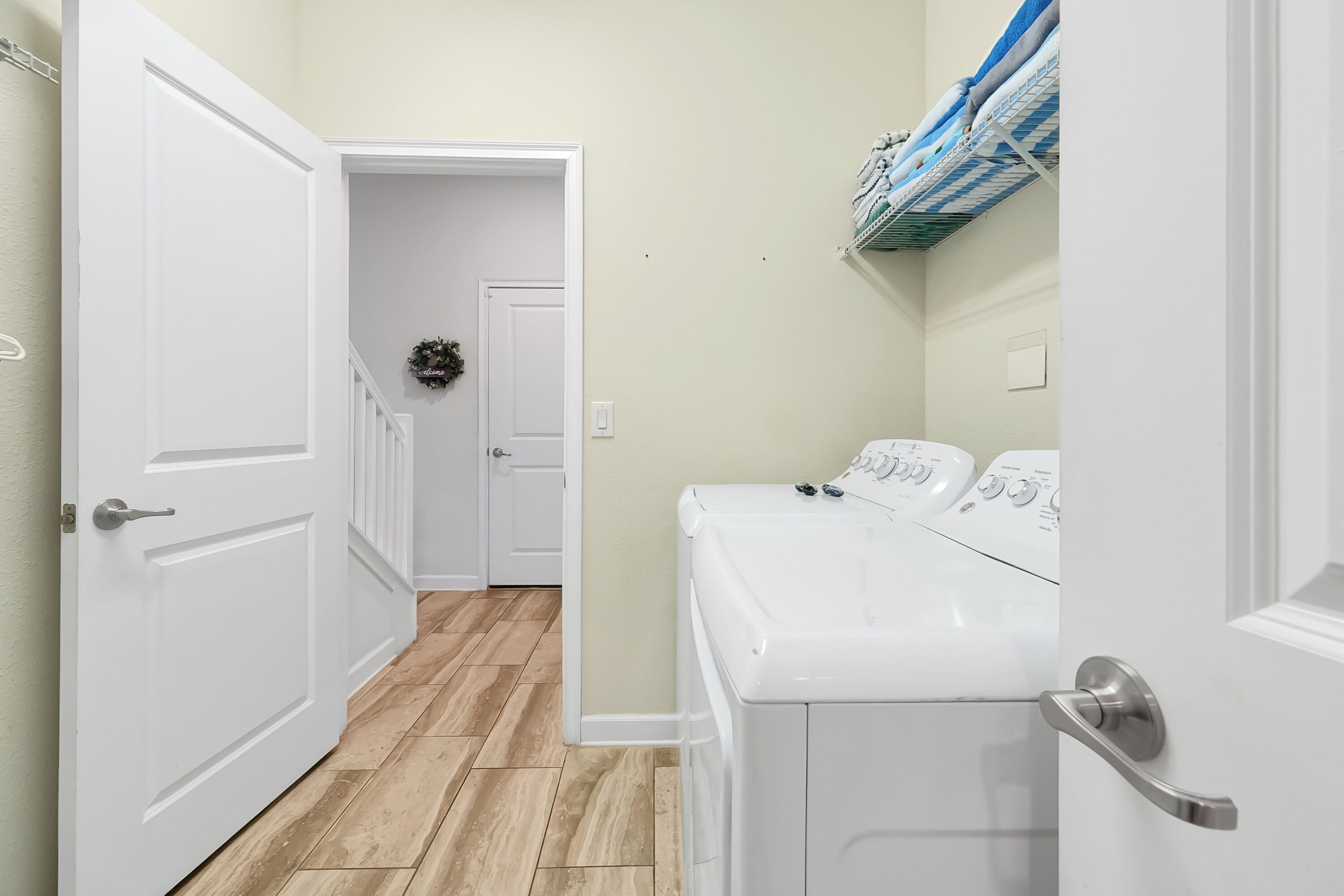 A laundry room with a washing machine, a dryer, and a rack with folded clothes.