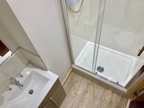 A bathroom with a shower, a sink, and wooden flooring. - Inverness Guest House (Inverness)