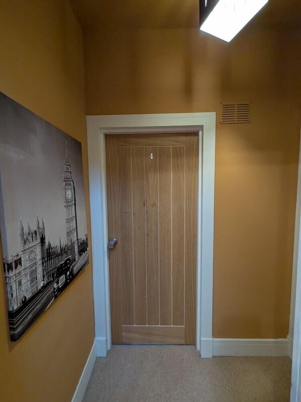 A hallway with a door marked '4', a painting of a cityscape, and a vent on the wall.