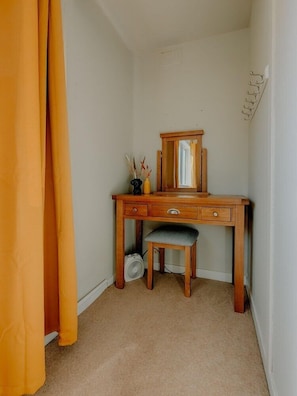A corner room with a wooden desk, a chair, a small fan, and a mirror.