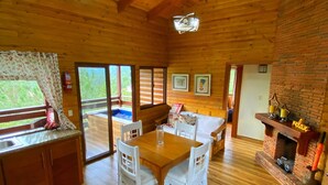 L’intérieur d’un chalet en bois, avec une table à manger, des chaises blanches, une cheminée et une vue à travers la porte.