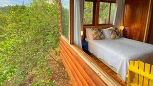 Une chambre avec un lit, un ventilateur de plafond et une vue sur la verdure.