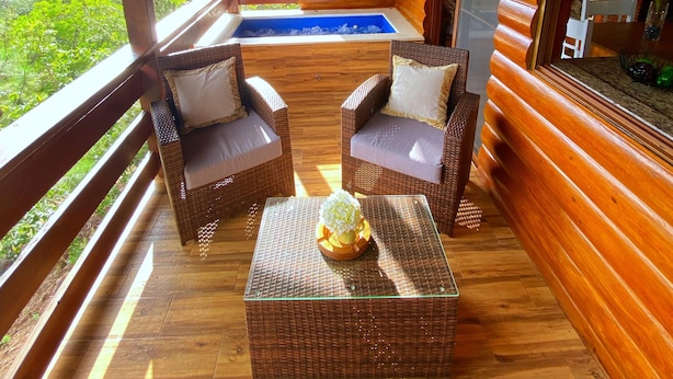 Une terrasse en bois, meublée de meubles en osier, avec une table à plateau de verre et une vue sur le paysage.
