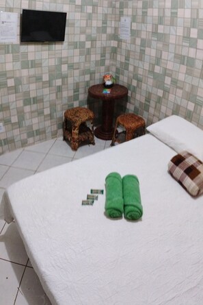 A hotel room with a bed, two small animal-shaped footstools, a round table, and a television mounted on the wall.
