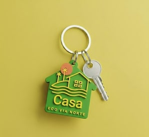 A keychain with a house-shaped key holder labeled 'Casa' and 'ECO VIA NORTE' on a yellow background. - Eco Via Norte House - MCZ (Maceió)