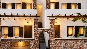 Un edifici amb façana de pedra, persianes de fusta i un rètol que diu 'Aelia Suites'.