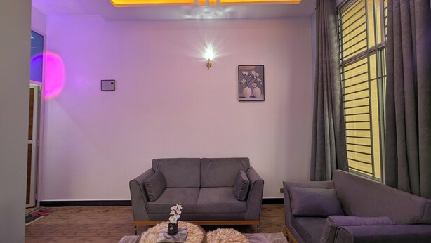 Ein Wohnzimmer mit grauem Sofa, zwei runden Beistelltischen, einer Wanddekoration und einem Fenster mit Jalousien.