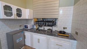 Eine Küche mit weißen Schränken, einer Mikrowelle, einem Kühlschrank und einem Fenster mit Jalousien.