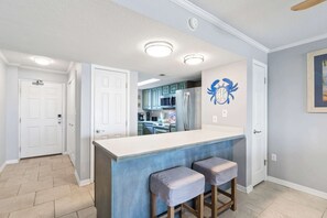 A modern kitchen with a central island, two bar stools, and a decorative wall piece. - Big Surf 1E & 2D - Gulf View, Beach, Pool, and Fun (Gulf Shores)