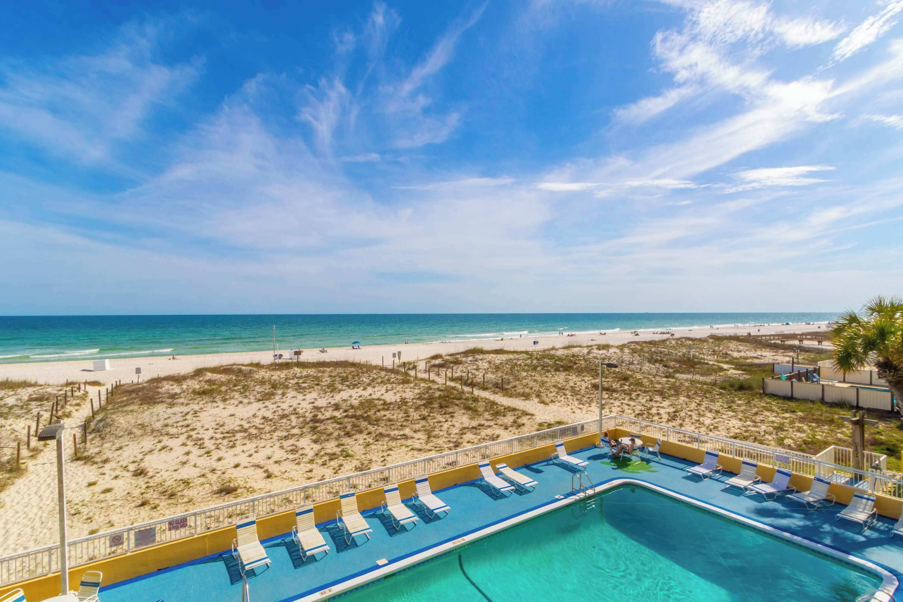 A pool area with lounge chairs, a clear view of the beach, and a sandy landscape.