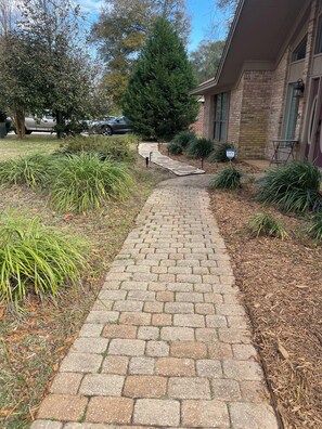 Un sendero pavimentado que conduce a un edificio de ladrillo con un pequeño espacio de asientos al aire libre.