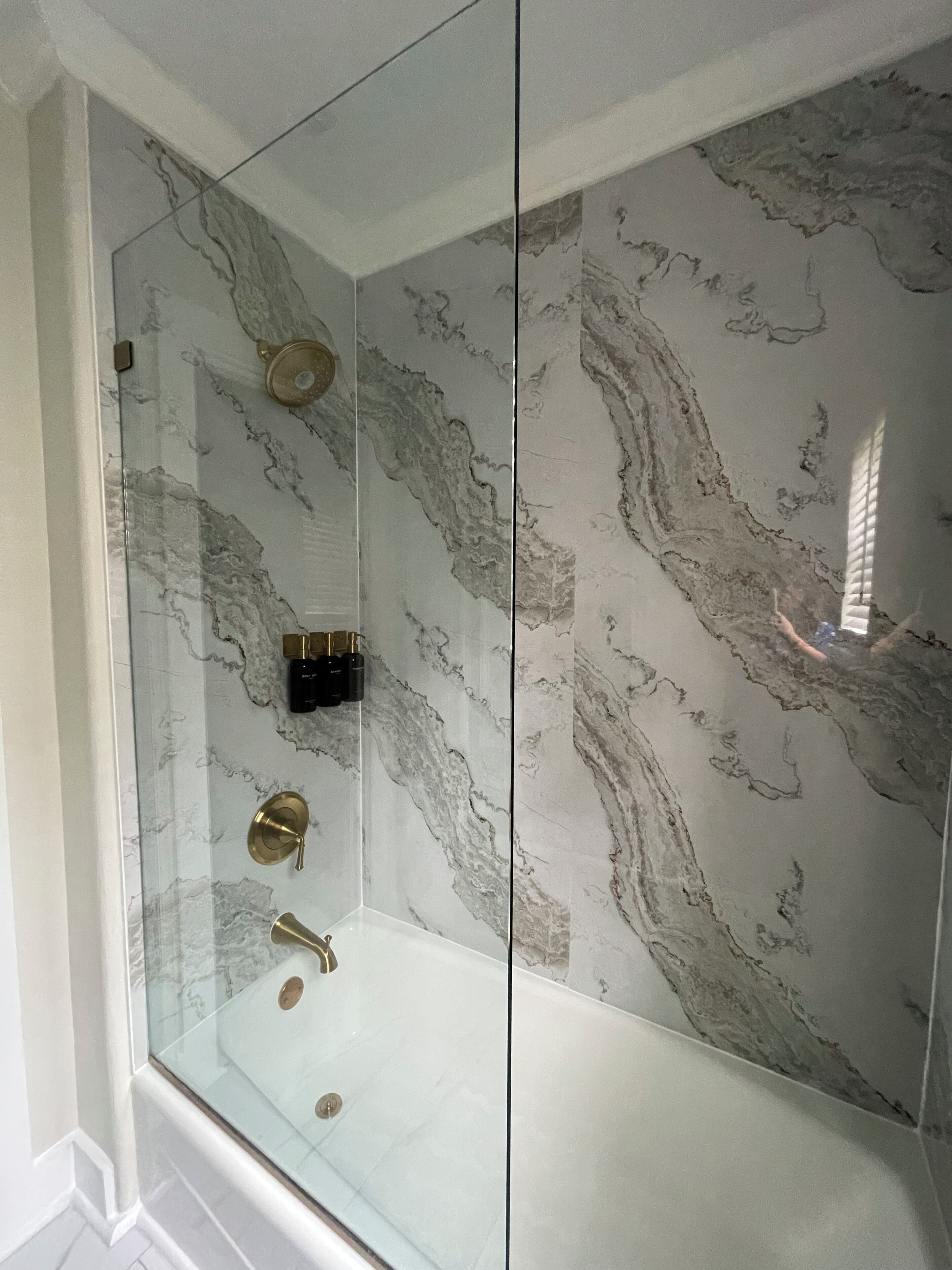 A glass-enclosed shower with marble walls, a gold showerhead, and a control panel.
