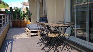 A balcony with a table and chairs, a wooden bench, and a view of the surrounding buildings. - Cosy Corner (Villeneuve-Loubet)
