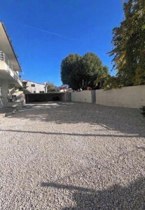 A gravel driveway leading to a building with a white facade and a balcony. - Cosy Corner (Villeneuve-Loubet)