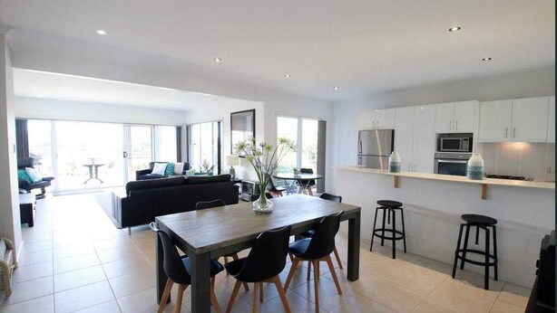 Une cuisine moderne avec des meubles blancs, une table à manger en bois et des tabourets de bar noirs.