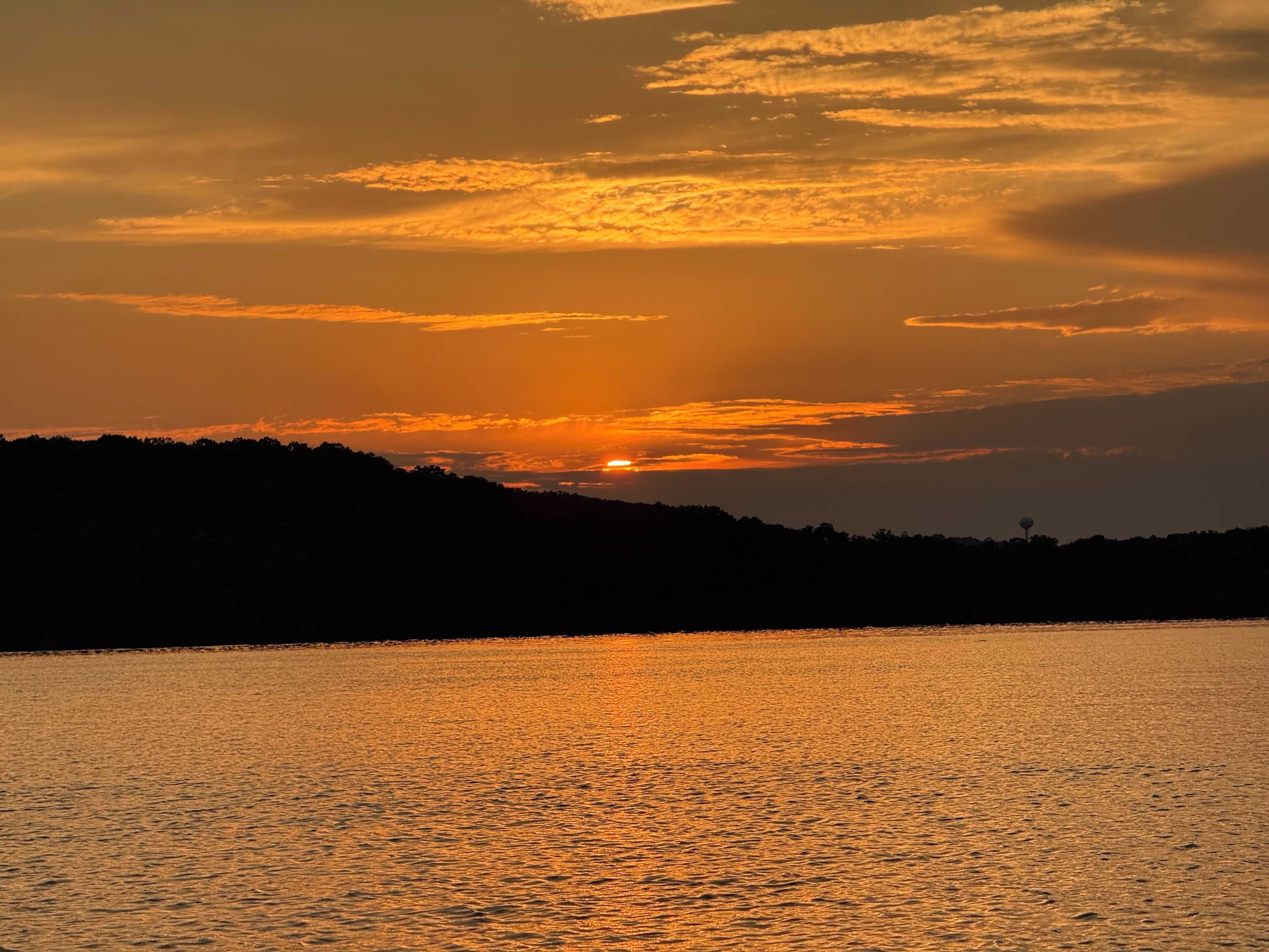 Tramonto su uno specchio d'acqua, con la sagoma di una collina e una struttura in lontananza.