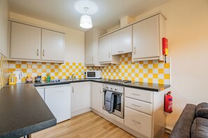 Une cuisine de taille réduite avec des meubles blancs, un four à micro-ondes, une cuisinière et un dosseret à carreaux.