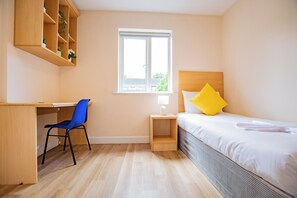 Une chambre à coucher comprenant un lit, un bureau, une chaise, une table de chevet, une fenêtre et une étagère en bois ornée de plantes.
