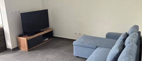 Una sala de estar moderna con un sofá seccional, un televisor de pantalla plana sobre un soporte de madera y piso de baldosas.