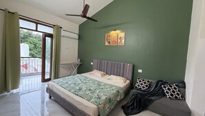 Quarto com cama, um banquinho, ventilador de teto, janela com cortinas e ar condicionado fixado na parede.