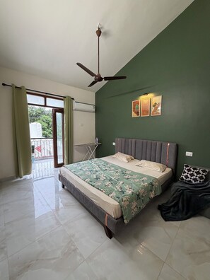 Une chambre à coucher avec un lit, un ventilateur de plafond, une fenêtre avec des rideaux et un balcon.