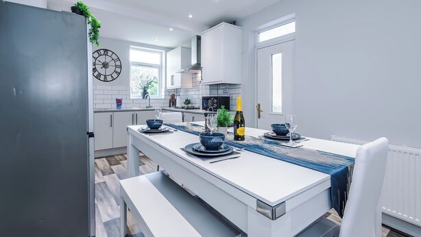 A modern kitchen with white cabinetry, a built-in oven, and a dining area with a white table set for two. - Neat 4BR House | Pool Table | Free Parking (Greater Manchester)
