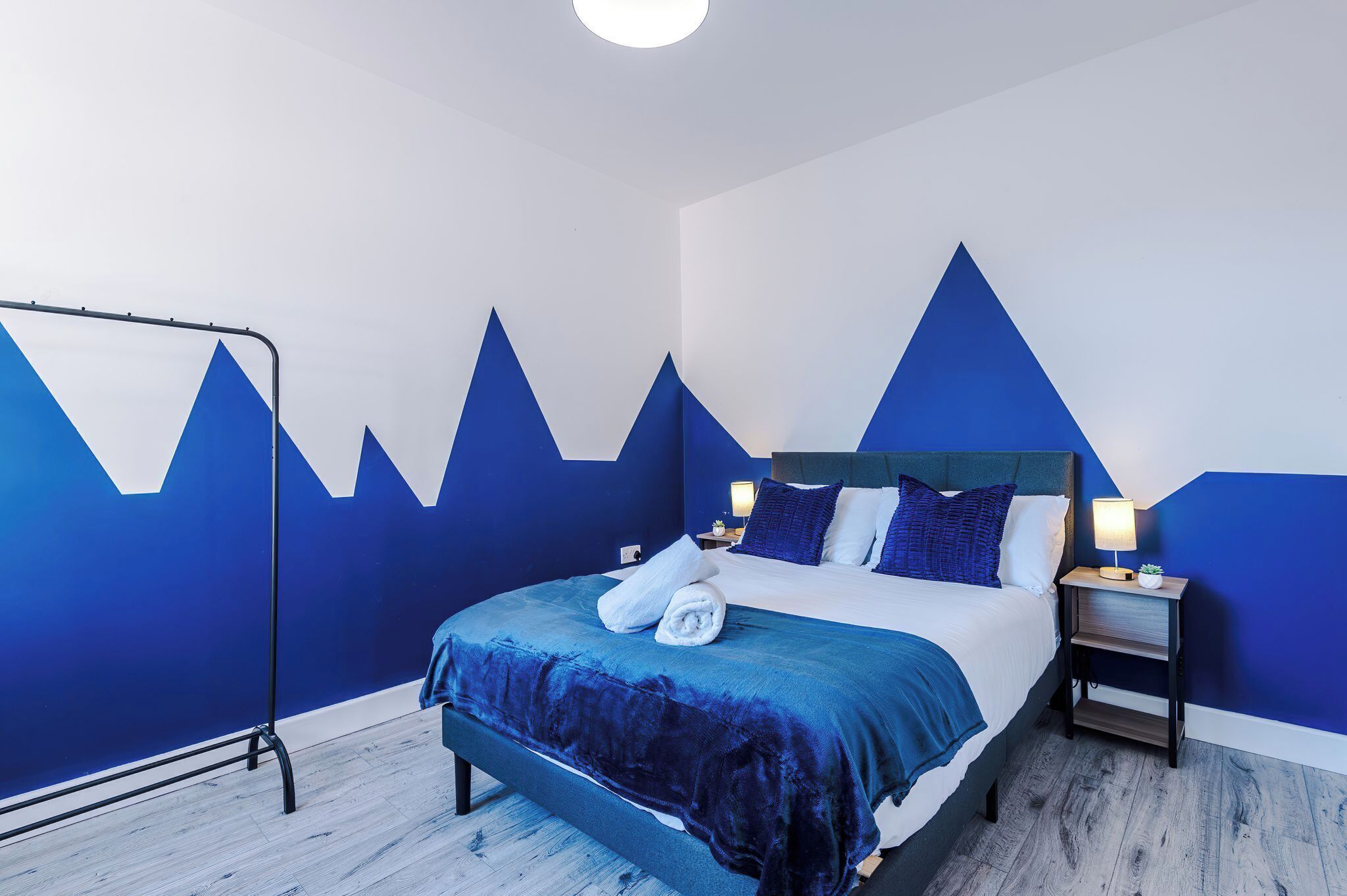 A bedroom with a bed, bedside tables, and a wall with mountain designs.