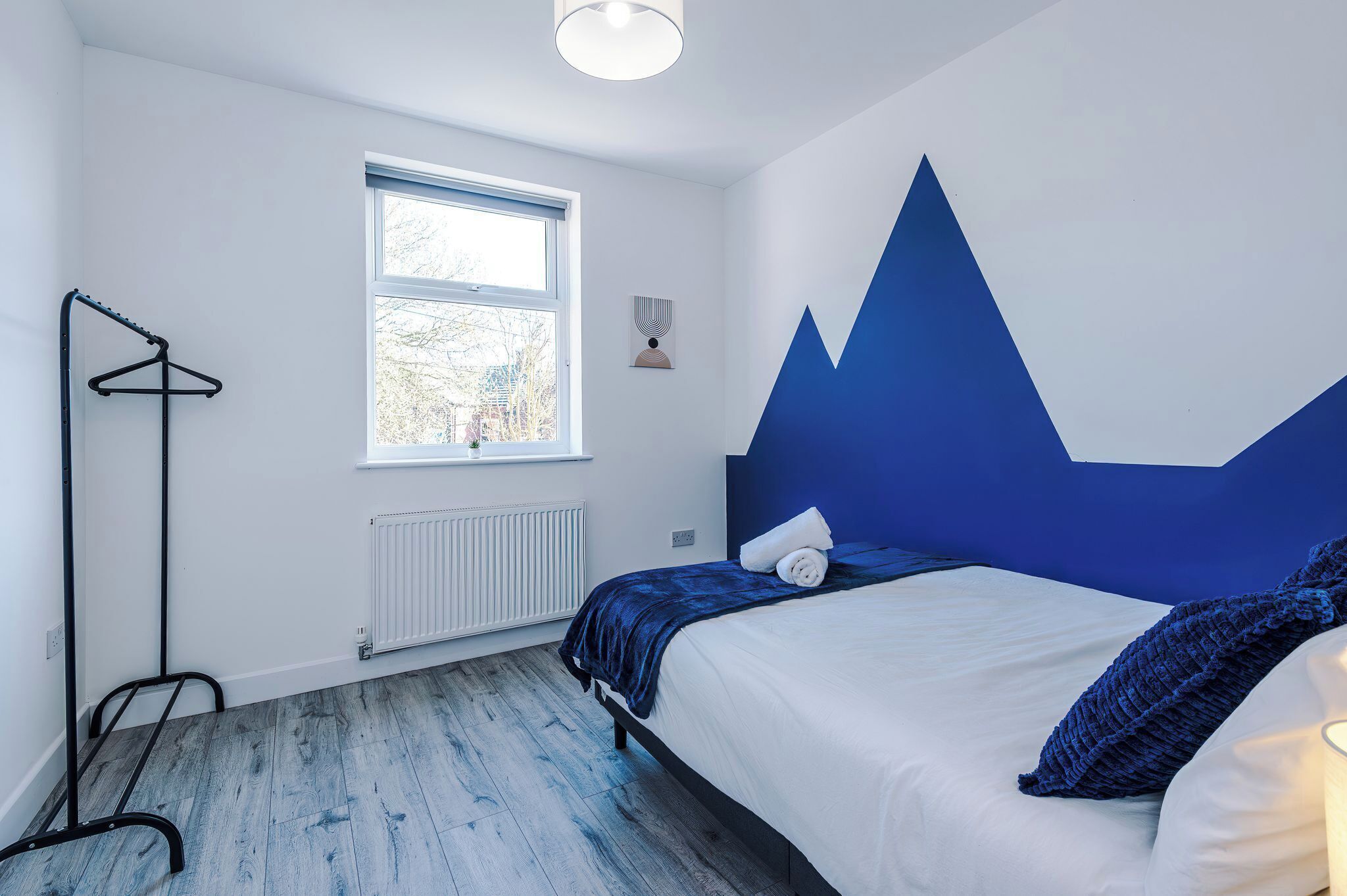 A bedroom with a bed, a radiator, a window, and a wall-mounted coat rack.