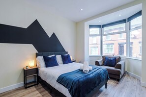 Ein modernes Hotelzimmer mit einem großen Bett, einer Couch, einem Nachttisch und einem Fenster mit Blick auf Gebäude.