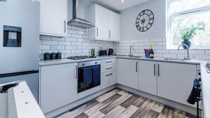 A modern kitchen with white cabinets, a built-in oven, a water dispenser, and a clock on the wall. - Neat 4BR House | Pool Table | Free Parking (Greater Manchester)